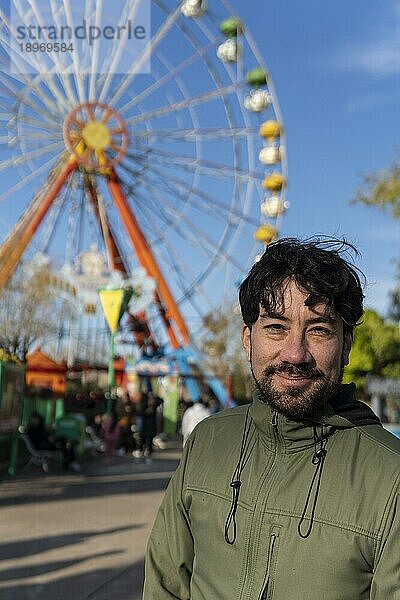 Porträt eines Latinomannes in einem Vergnügungspark  der glücklich mit dem Riesenrad im Hintergrund posiert