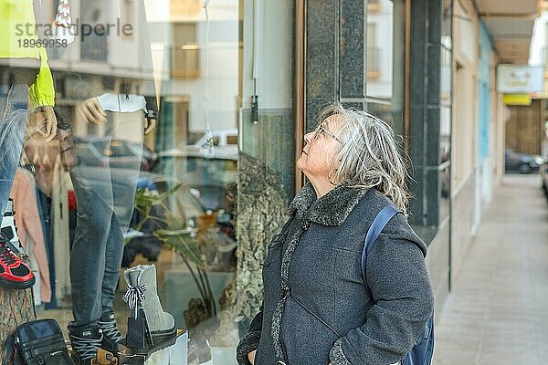 Ronda  Málaga  Spanien Ältere Frau mit weißem Haar und Mantel und Einkaufstüten schaut in ein Schaufenster