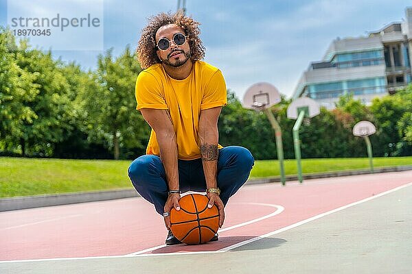 Porträt eines afro haarigen Mannes in einem gelben TShirt mit einem Basketball. Porträt auf einem Basketballplatz in der Stadt