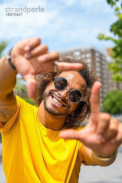 Porträt eines afro haarigen Mannes in einem gelben T Shirt. Porträt in der Stadt lächelnd im Sommerurlaub