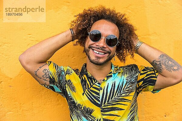 Attraktiver Mann mit Afrohaar im Sommer in einem Palmenhemd auf gelbem Hintergrund