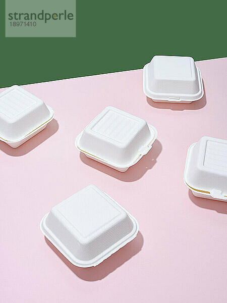 Take-Out-Boxen für Burger vor einem grünen und rosa Hintergrund
