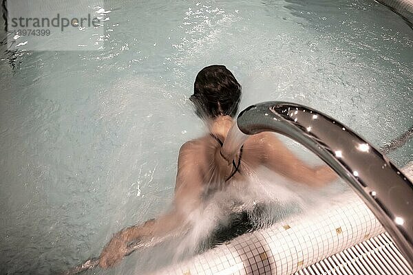 Frau entspannt sich in einem Hydro Massage Pool mit fallendem Wasser auf ihre Wirbelsäule und ihren Nacken in der Schweiz