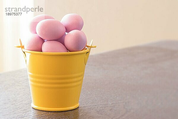 Gelber Eimer mit violetten Ostereiern auf einem Tisch