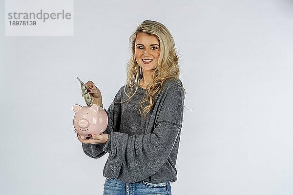 Ein wunderschönes blondes Modell hält ein Sparschwein und spart Geld