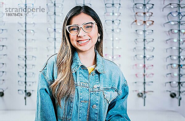 Lächelndes glückliches Mädchen mit Brille mit Brillengeschäft Hintergrund  Porträt eines glücklichen Mädchens mit Brille in einem Brillengeschäft