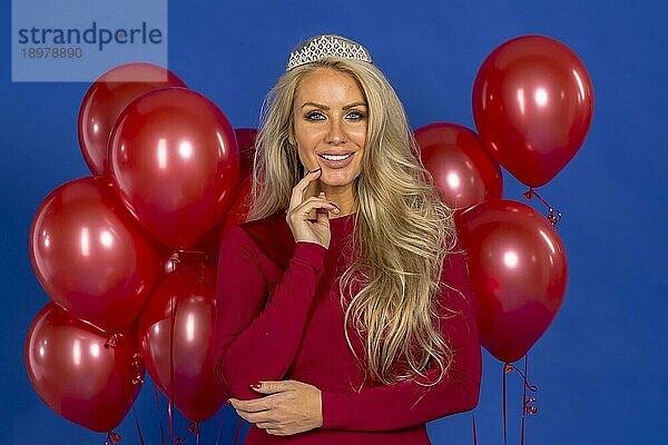 Ein schönes blondes Modell posiert mit einem Diadem und roten Luftballons vor der Kamera in einer Studioumgebung
