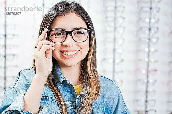 Lächelnde schöne Mädchen Modellierung Brille in einem optischen Geschäft. Glückliche Teenagermädchen in Brillen mit Shop Brillen Hintergrund