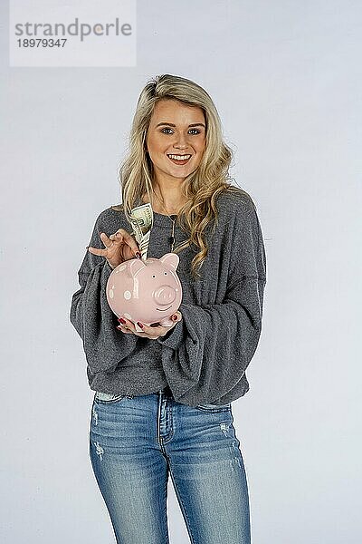 Ein wunderschönes blondes Modell hält ein Sparschwein und spart Geld