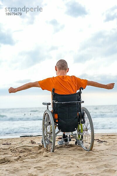 Eine behinderte Person auf dem Rücken in einem Rollstuhl am Strand fühlt sich frei