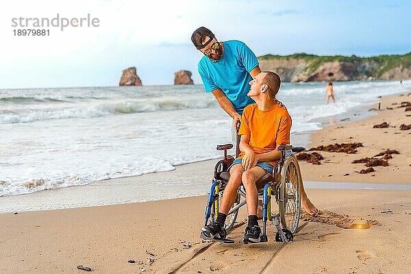 Eine behinderte Person im Rollstuhl am Strand  geschoben von einem Freund am Meer  genießt den Sommer