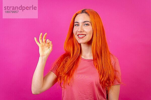 Rothaarige Frau im Studio Fotografie macht die ok Geste auf einem rosa Hintergrund