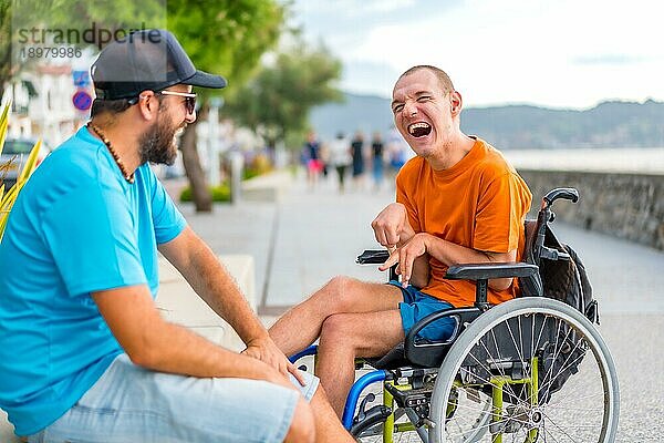 Ein behinderter Mensch im Rollstuhl mit einem Freund im Sommerurlaub am Meer  der viel lacht