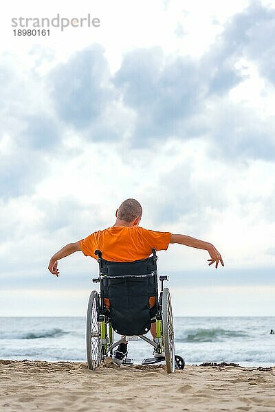 Ein Behinderter in einem Rollstuhl auf dem Rücken am Strand im Sommer mit Blick auf das Meer