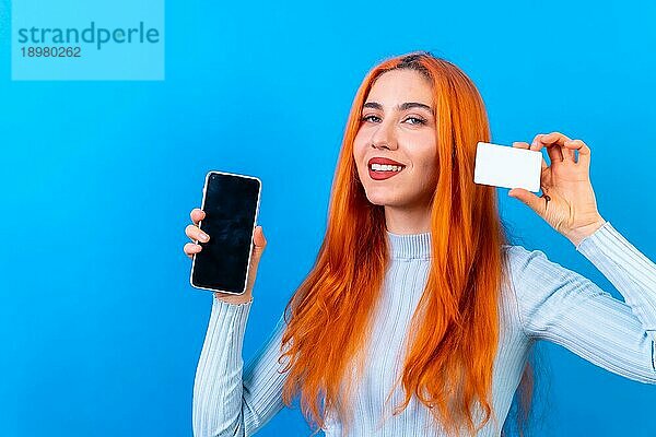 Rothaarige Frau im Studio Fotografie Online Zahlung mit Handy auf einem blauen Hintergrund