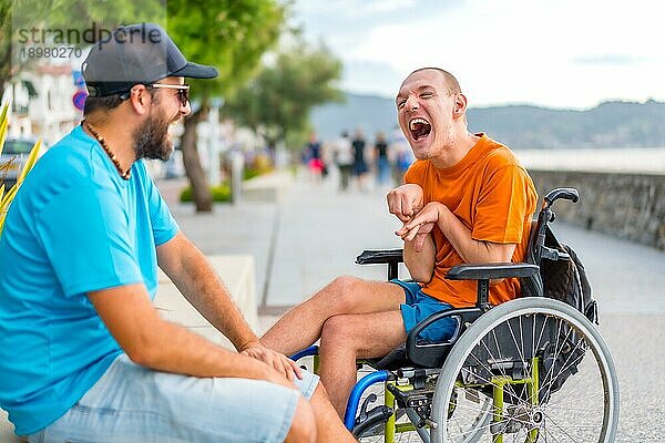 Ein behinderter Mensch im Rollstuhl mit einem Freund in den Sommerferien  der sich amüsiert und viel lacht