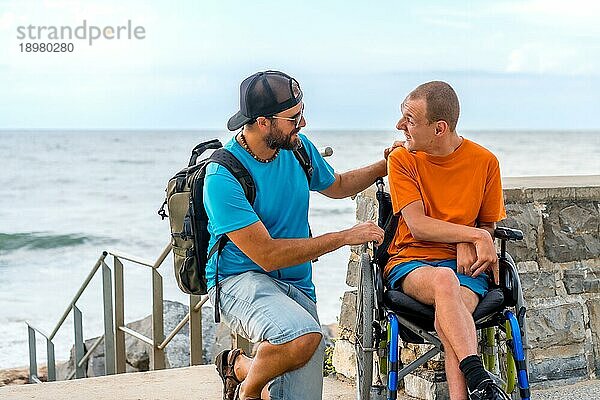 Eine behinderte Person im Rollstuhl mit einem Freund im Sommerurlaub  die sich am Meer unterhalten