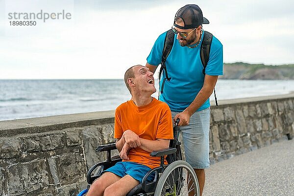 Eine behinderte Person im Rollstuhl wird von einem Freund auf der Strandpromenade geschoben und hat Spaß im Sommer