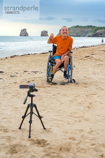 Porträt einer behinderten Person im Rollstuhl am Strand  die ein Video aufnimmt