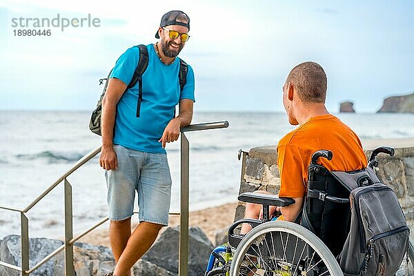 Eine behinderte Person im Rollstuhl mit einem Freund im Sommerurlaub am Meer