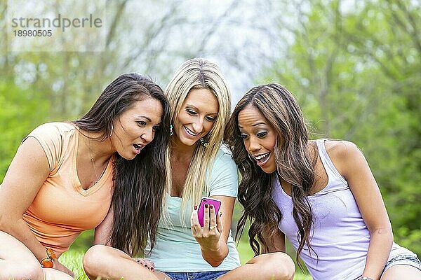 Drei junge Frauen  die einen Tag im Park mit ihren Handys genießen