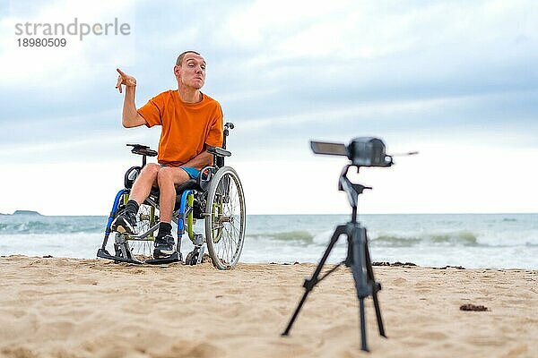 Porträt einer behinderten Person im Rollstuhl am Strand bei der Aufnahme eines Videoclips