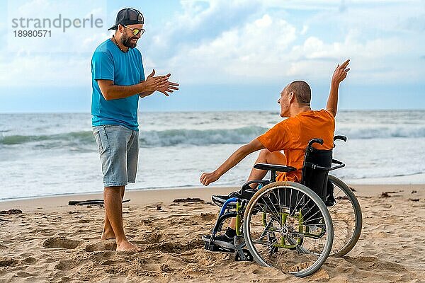 Eine behinderte Person im Rollstuhl am Strand mit einem Freund  der Spaß am Tanzen hat