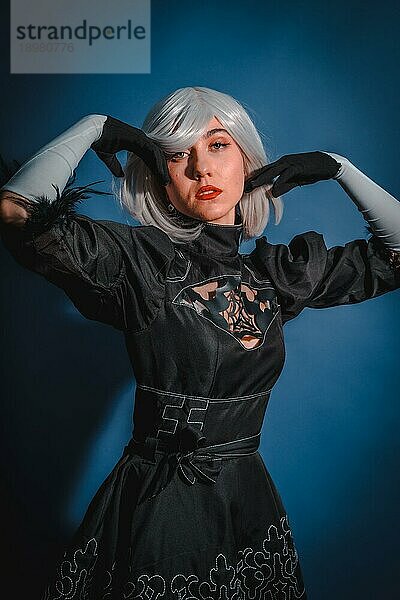 Porträt einer Cosplay Frau in einem schwarzen Kostüm und einer weißen Perücke im Studio auf blauem Hintergrund