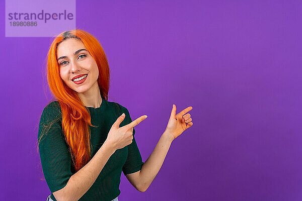 Rothaarige Frau in Studiofotografie macht die Geste des Zeigens auf einem lila Hintergrund