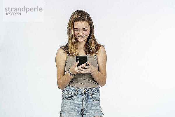 Ein schönes blondes Teenager Model spielt mit ihrem Handy in einer Studioumgebung