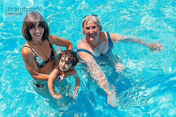 Mutter und Großmutter amüsieren sich mit ihrem Enkel im Schwimmbad im Sommerurlaub