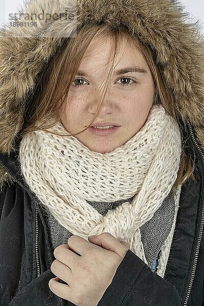 Ein schönes blondes Teenager Model posiert mit einem Wintermantel in einer Studioumgebung