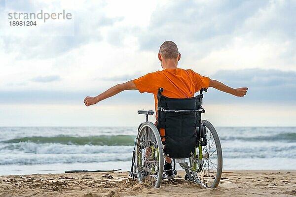 Eine behinderte Person auf dem Rücken in einem Rollstuhl am Strand fühlt sich frei