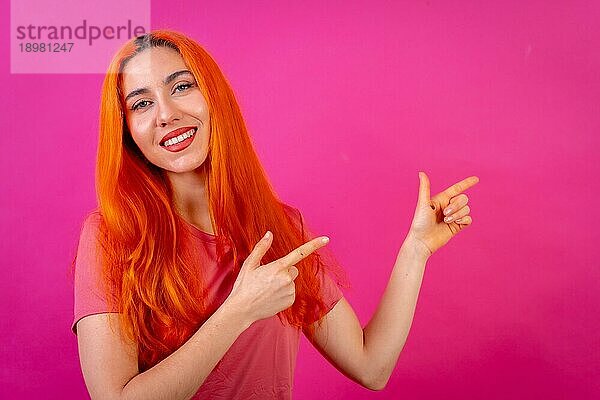 Rothaarige Frau im Studio Fotografie macht die Geste des Zeigens auf einem rosa Hintergrund