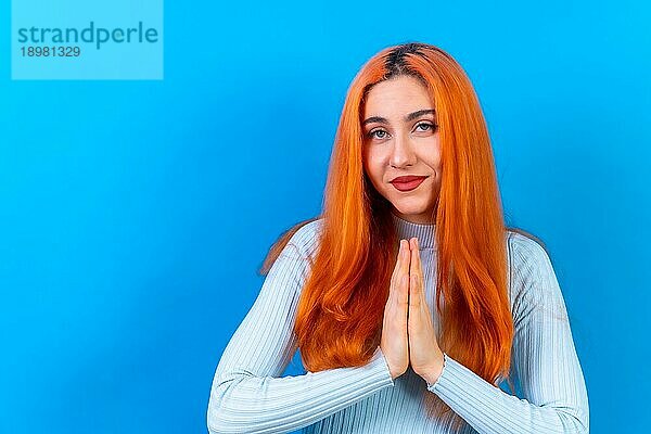 Rothaarige Frau im Studio Fotografie macht die Geste bitte auf einem blauen Hintergrund