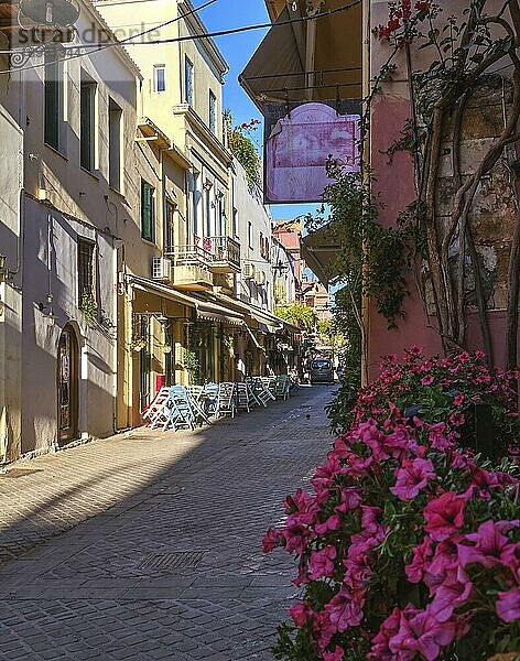 Schöner Blick auf die engen Gassen der Altstadt von Chania  Kreta  Griechenland  am frühen Morgen. Cafés und Restaurants sind bereit  zu öffnen. Selektiver Fokus. Satte rosa Petunienblüten im Vordergrund  Europa