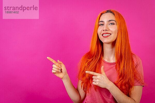 Rothaarige Frau im Studio Fotografie macht die Geste des Zeigens auf einem rosa Hintergrund