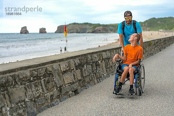 Eine behinderte Person im Rollstuhl wird von einem Freund am Strand geschoben und hat Spaß im Sommer