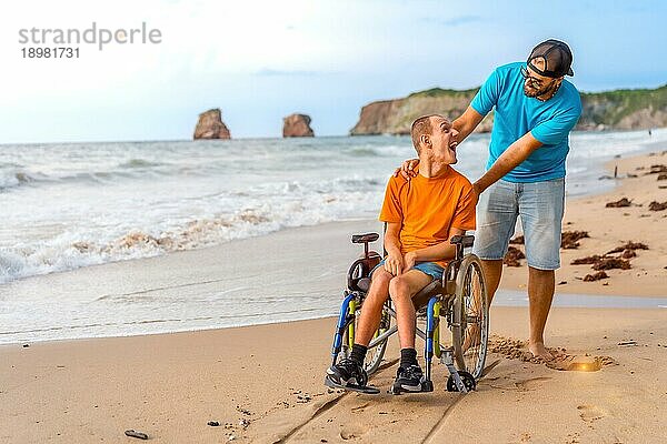 Eine behinderte Person im Rollstuhl am Strand  geschoben von einem Freund am Meer