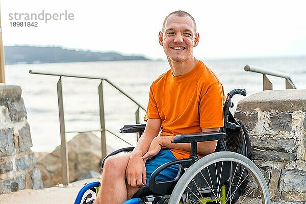 Porträt einer behinderten Person in einem Rollstuhl am Strand im Sommerurlaub lächelnd