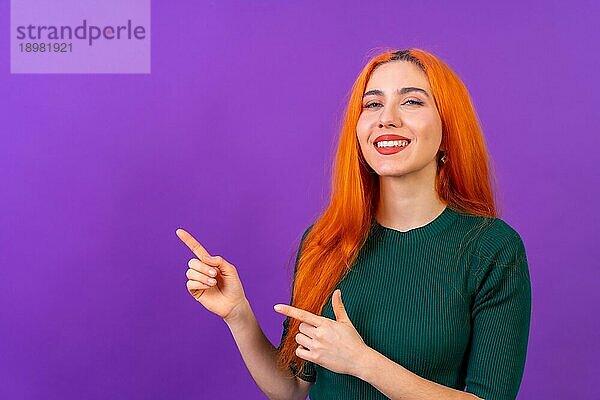 Rothaarige Frau in Studiofotografie macht die Geste des Zeigens auf einem lila Hintergrund