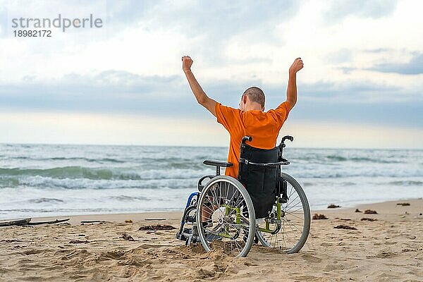 Behinderte Person auf dem Rücken in einem Rollstuhl am Strand mit offenen Armen  die die Freiheit genießen
