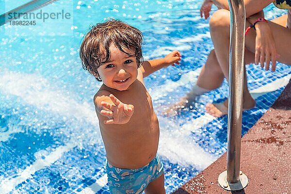 Zweijähriger Junge  der den Sommer im Schwimmbad genießt und lächelnd in die Kamera schaut
