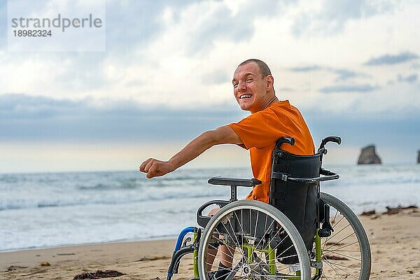 Eine behinderte Person auf dem Rücken in einem Rollstuhl am Strand im Sommer am Meer