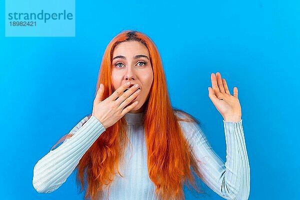 Rothaarige Frau in Studiofotografie macht die erstaunliche Geste auf einem blauen Hintergrund