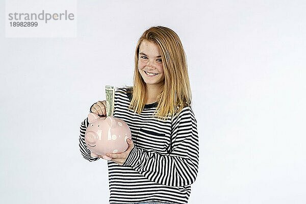 Ein wunderschönes blondes Teenagermodell das ein Sparschwein hält und Geld spart