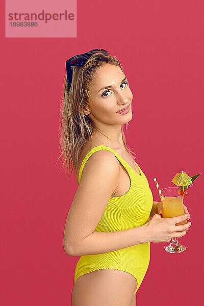 Attraktive trendige blonde Frau mit exotischen tropischen Cocktail in einem Glas heben ihre Sonnenbrille auf den Kopf  wie sie lächelt in die Kamera Konzept der Sommerurlaub