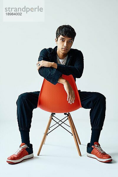Stylish gut aussehend junger Mann posiert auf Studio sitzt auf einem Stuhl Blick in die Kamera auf weißem Hintergrund. Mann Schönheit Konzept