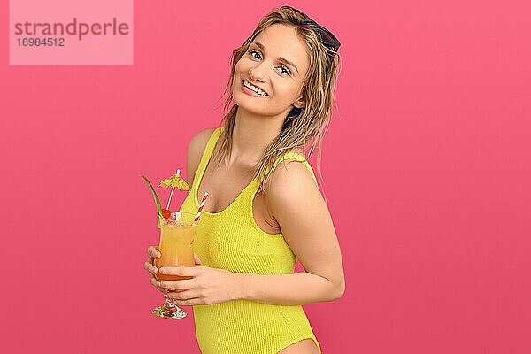 Attraktive trendige blonde Frau mit exotischen tropischen Cocktail in einem Glas heben ihre Sonnenbrille auf den Kopf  wie sie lächelt in die Kamera Konzept der Sommerurlaub