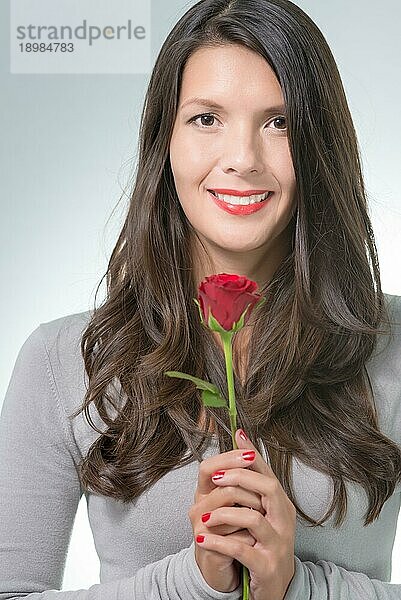 Attraktive Frau mit langem brünetten Haar hält eine langstielige rote Rose  ein Geschenk von einem geliebten Menschen zum Valentinstag oder Geburtstag